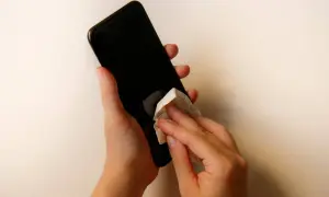 Dłonie czyszczą ekran telefonu chusteczką. Dowiedz się, czym wyczyścić ekran telefonu, by był lśniący i bez smug.