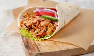 Domowy kebab w tortilli z mięsem, sałatą, pomidorem, ogórkiem i cebulą na desce.