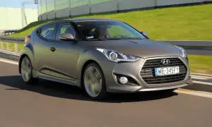 Szary Hyundai Veloster pędzi po drodze, za nim zielone ekrany dźwiękochłonne.