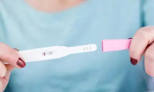 Dłoń trzyma test ciążowy z widocznym jednym paskiem. Rozważana jest opcja przerwania ciąży, być może z użyciem mizoprostolu.
