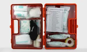 Wyposażenie apteczki w zakładzie pracy rozporządzenie: pomarańczowa walizka z materiałami opatrunkowymi, plastrami, bandażami, rękawicami i instrukcją.