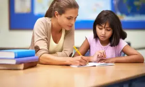 Nauczycielka pomaga uczennicy w pisaniu, wspierając ją w procesie edukacyjnym, który może być częścią orzeczenia z poradni psychologiczno-pedagogicznej.