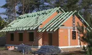 Dom w budowie, widoczny system gospodarczy budowa dachu z zielonych krokwi. Na placu budowy materiały budowlane.
