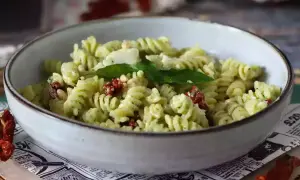 En skål med kall pastasallad med pesto, soltorkade tomater och pinjenötter. En perfekt sommarrätt.