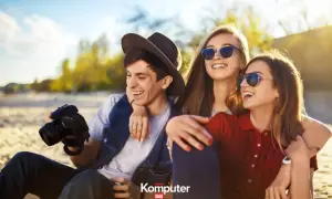 Trzech przyjaciół na plaży, jeden z aparatem, śmieją się. Dowiedz się, jak poprawić jakość zdjęcia, by uchwycić takie chwile.