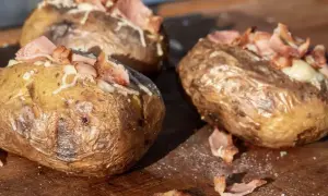 Pyszne ziemniaki z grilla, zapieczone z serem i chrupiącym boczkiem, kuszą na drewnianej desce.