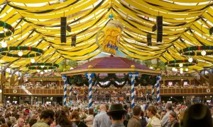 Un'enorme tenda gialla e nera, dove si svolge l'Oktoberfest, piena di gente, con un gigantesco boccale di birra sopra un palco.