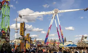 Voller Rummelplatz mit Achterbahn, einem riesigen Pendel und vielen Menschen. Im Hintergrund ragt der Hamburger Fernsehturm auf.