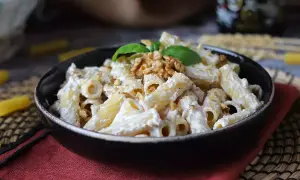 Makaron penne z kremowym sosem, orzechami włoskimi i bazylią w czarnej misce.