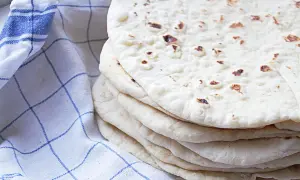 En hög med hemgjorda tortillas, perfekta för ditt nästa tortilla recept. En blårutig kökshandduk ligger bredvid.