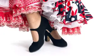 Zapatos negros de tacón y medias de rejilla, listos para el zapateo flamenco entre volantes de lunares y encaje.