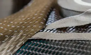 Fascio di filamenti dorati, forse fibra di basalto, cuciti con filo bianco, sovrapposti a tessuti a trama fitta.