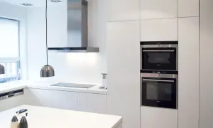 Nowoczesna kuchnia z białymi frontami do szafek kuchennych, stalowym okapem i wbudowanymi piekarnikami.