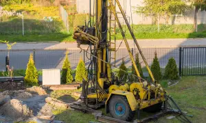 Żółta wiertnica na podwórku, przygotowana do wiercenia studni głębinowej. Koszt takiej inwestycji może być różny.