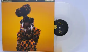 Little Simz, czasem introvert, na okładce płyty "Sometimes I Might Be Introvert". Obok przezroczysta winylowa płyta.