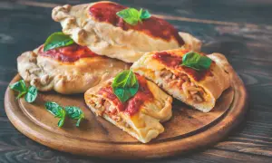 En stapel gyllene calzoner toppade med tomatsås och färsk basilika. En calzone är uppskuren och visar en fyllning av kött och grönsaker. Perfekt för den som vill veta mer om calzone kalorier.
