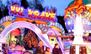 Bunte Lichter und Piratenmotive auf einer Kirmes in Berlin. Eine Achterbahn mit dem Schriftzug "Sky Krake" zieht Besucher an.