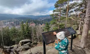 Dziecko z czapką w kształcie uszek kota przygląda się mapie szlaków w Karkonoszach. Widok na Karpacz i góry.