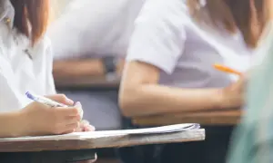 Dłoń studenta pisząca długopisem na kartce papieru podczas egzaminu.