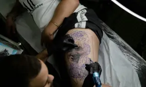 Un tatuador trabaja en un retrato en la pierna de un cliente, demostrando la habilidad de los mejores tatuadores de España.