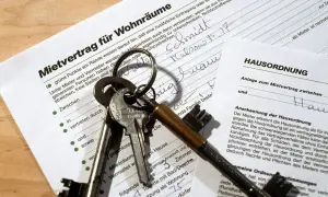 Schlüsselbund liegt auf einem Mietvertrag und einer Hausordnung. Der Text "Mietvertrag nicht unterschreiben" ist nicht direkt sichtbar, aber die Dokumente deuten auf eine Wohnungsanmietung hin.