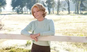 Diane Lane w pastelowym sweterku opiera się o płotek, przypominając scenę z jednego z jej filmów.