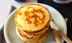 Stapel goldbrauner Dinkel Pancakes mit einem Muster auf dem obersten Pancake, serviert auf einem hellblauen Teller mit Messer und Gabel.