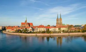 Widok na Ostrów Tumski, serce wrocławskiej starówki, z katedrą i innymi zabytkowymi budynkami odbijającymi się w spokojnej wodzie.