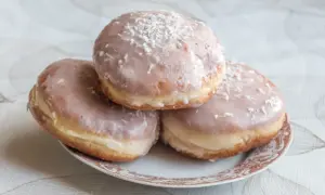 Trzy pączki z lukrem do pączków i wiórkami kokosowymi na talerzyku.