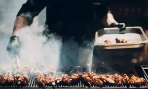 Fleischspieße brutzeln auf dem Grill, Rauch steigt auf. Ein Koch bereitet ein italienisches Grillfest vor.