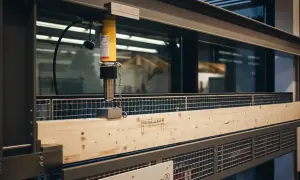 Test wytrzymałości belki drewnianej z ceownikiem. Hydrauliczny siłownik naciska na belkę, sprawdzając jej odporność.