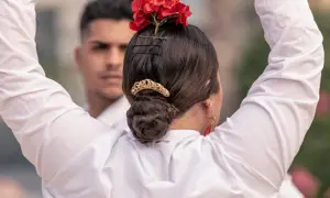 Peinados para bailar flamenco: moño bajo adornado con flores rojas y peineta dorada. Un hombre con camisa blanca al fondo.