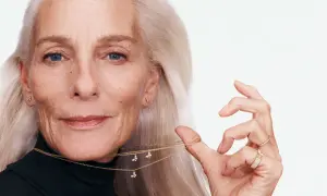Mujer mayor con cabello plateado, luciendo una medalla de la madre con forma de mariposa y anillos brillantes.
