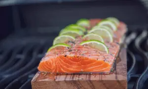 Ein saftiges Lachsfilet mit Limettenscheiben und Kräutern wird auf einem Zedernholzbrett gegrillt.