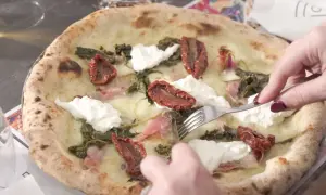 Una puccia Otranto, con pomodori secchi, burrata e verdure, viene tagliata con una forchetta.