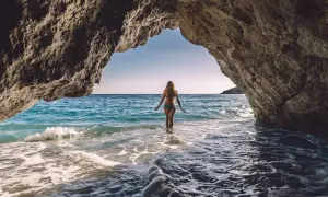 Kobieta wchodzi do turkusowej wody z jaskini. Idealne miejsce na wakacje all inclusive w Albanii.