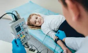 Uśmiechnięta dziewczynka leży na łóżku podczas badania EEG, które pomaga diagnozować padaczkę u dzieci.