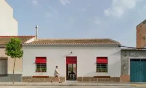 Fachada casa pueblo moderna con persianas rojas vibrantes y un hombre corriendo.