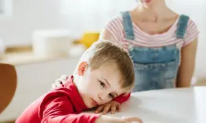 Smutny chłopiec z czerwonym sweterkiem, którego mama głaszcze po ramieniu. Może to być związane z chorobą, np. pandas.