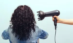 Donna con capelli ricci scuri viene asciugata con diffusore. Scopri come asciugare i capelli ricci per un risultato perfetto.