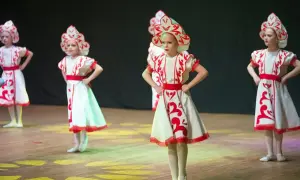 Niñas con trajes tradicionales bailan en un escenario de teatro.