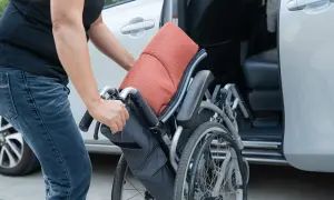 Persona piega una carrozzina vicino a un'auto, pensando all'assicurazione auto legge 104.