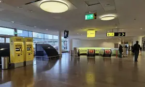 Dwie żółte kasy biletowe Arlanda Express, gdzie sprawdzisz arlanda express cena. Dalej schody ruchome i ludzie.