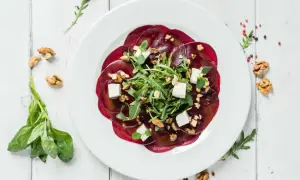 Rote Bete Carpaccio mit Rucola, Walnüssen und Feta auf einem weißen Teller, garniert mit frischem Basilikum.