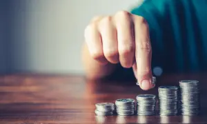 Mano che aggiunge una moneta a una pila, simboleggiando la crescita finanziaria, il risparmio o la gestione del **tutore e indennità di accompagnamento**.