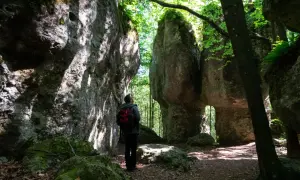 Ein Wanderer steht in einer **steinernen Stadt** aus Felsformationen, umgeben von üppigem Grün und Sonnenlicht.