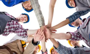 Zespół budowlańców zjednoczony w geście solidarności. Ich wspólne dłonie symbolizują siłę i współpracę, jakiej wymaga praca społecznego inspektora pracy.
