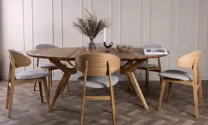 En elegant dukning runt ett ovalt träbord med sex stolar. En vas med torkade blommor, en ljusstake och en korg pryder bordet.