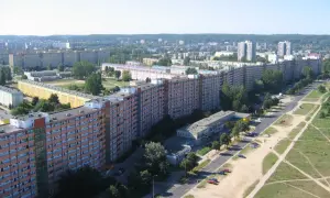 Długi, falisty budynek mieszkalny, znany jako falowiec gdańsk, rozciąga się wzdłuż ulicy, otoczony zielenią i innymi blokami.