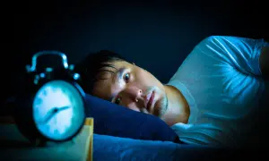 Hombre en cama, con ojos abiertos y alarma. Podría estar experimentando alucinaciones hipnagógicas.